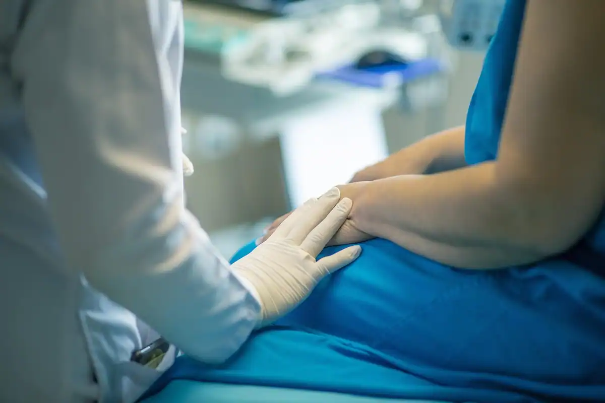 Medic cu mănuși de unică folosință care ține mâna unei paciente pe patul de spital