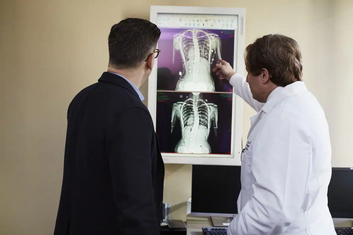 Doi medici arată o radiografie a coloanei unui pacient, înainte de decizie