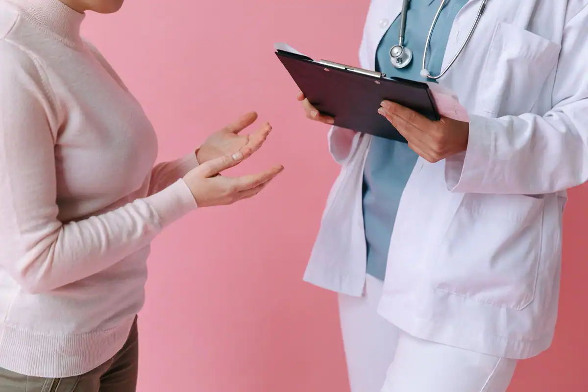 Medic în halat alb discută cu o pacientă, care ține o tabletă în mână