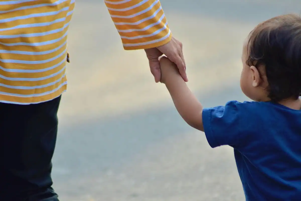 Adult ține de mână un copil mic, care merge alături de el