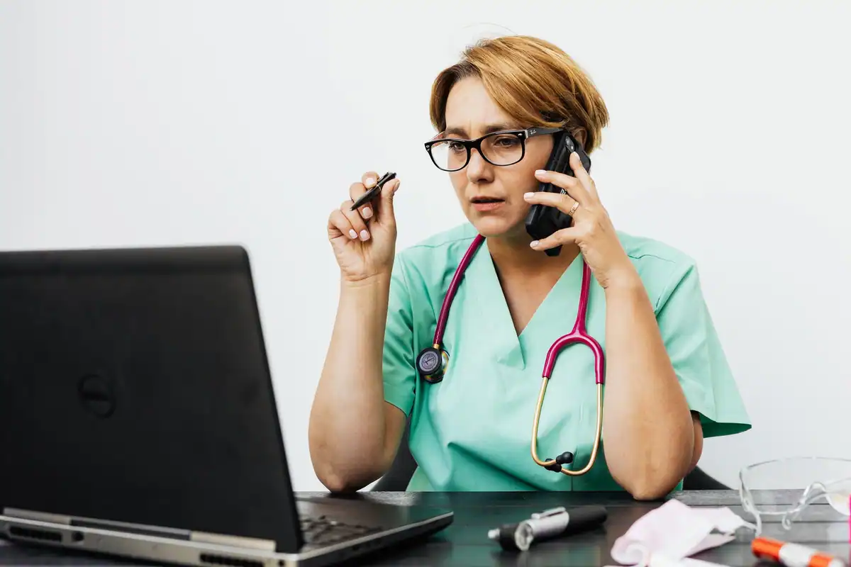 Asistentă în ținută verde vorbește la telefon în fața unui laptop