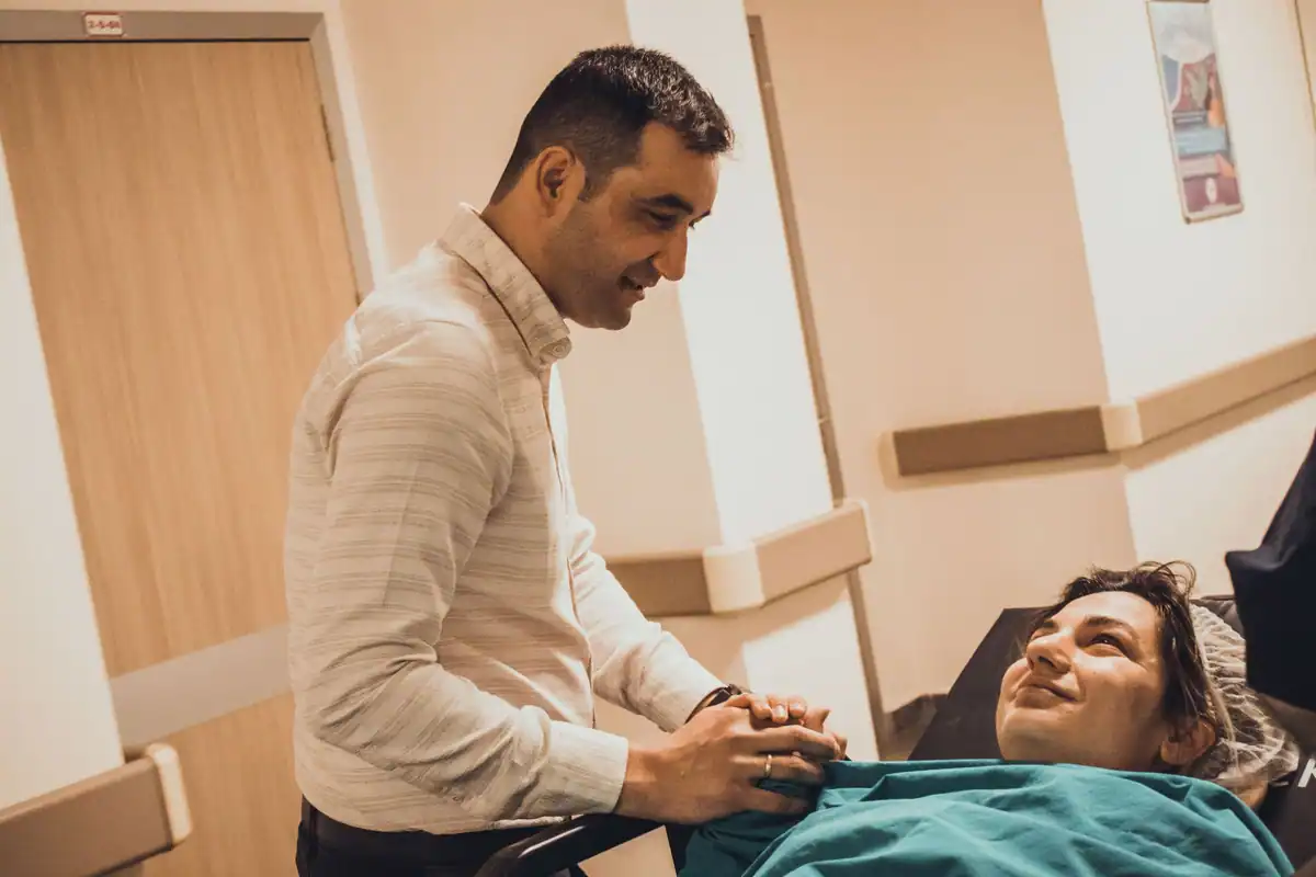 Bărbat se apleacă spre o pacientă zâmbitoare, în coridorul unui spital