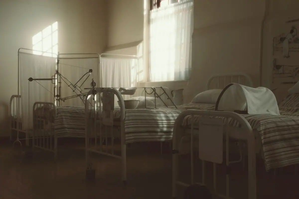 Salon vechi de spital cu paturi metalice, într-o lumină blândă