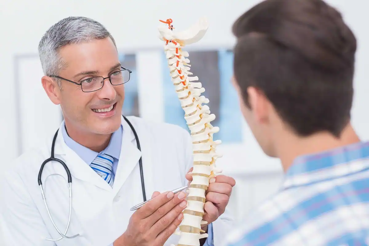 Medic arată pe un model al coloanei vertebrale unui pacient atent