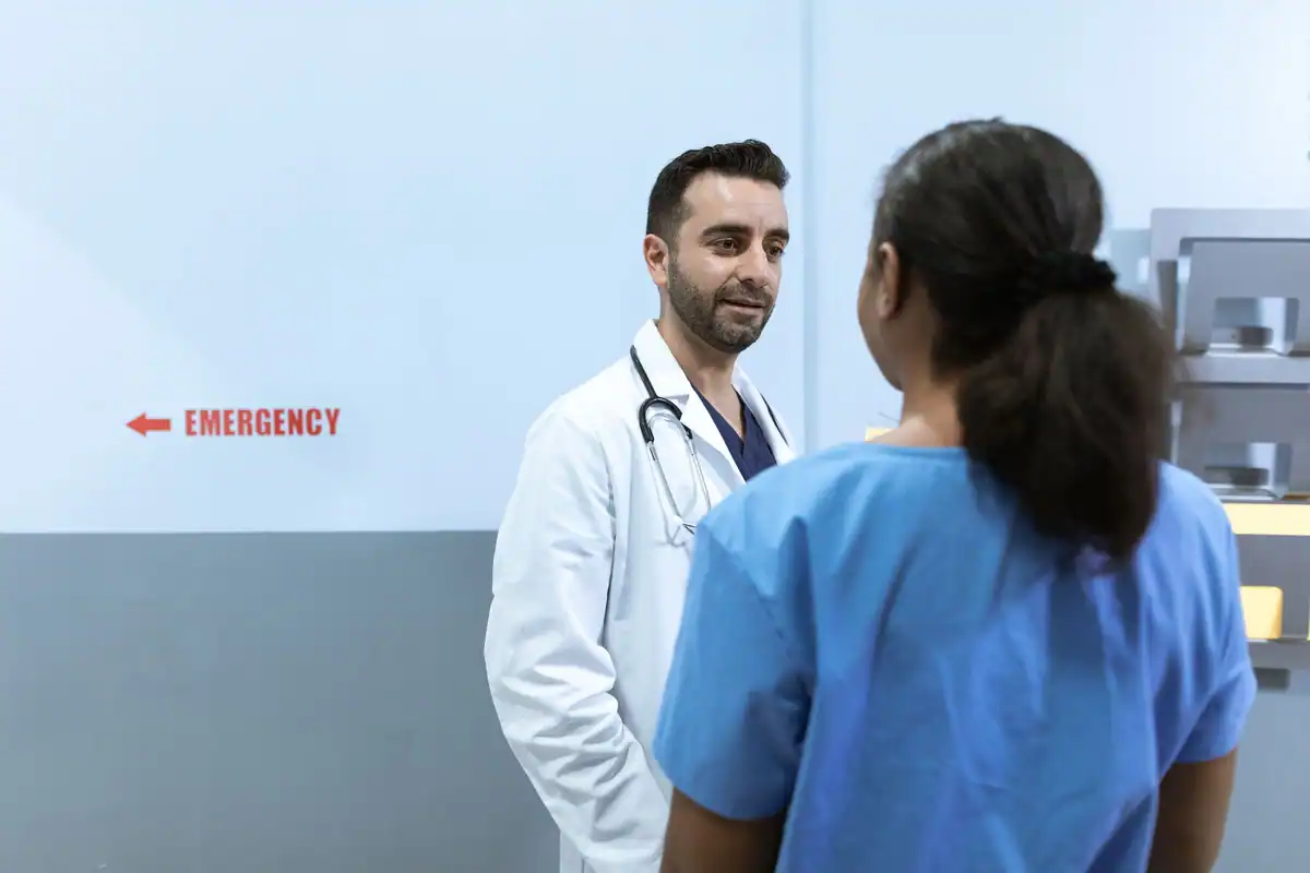 Medic în halat alb vorbește serios cu o asistentă, pe un hol de spital