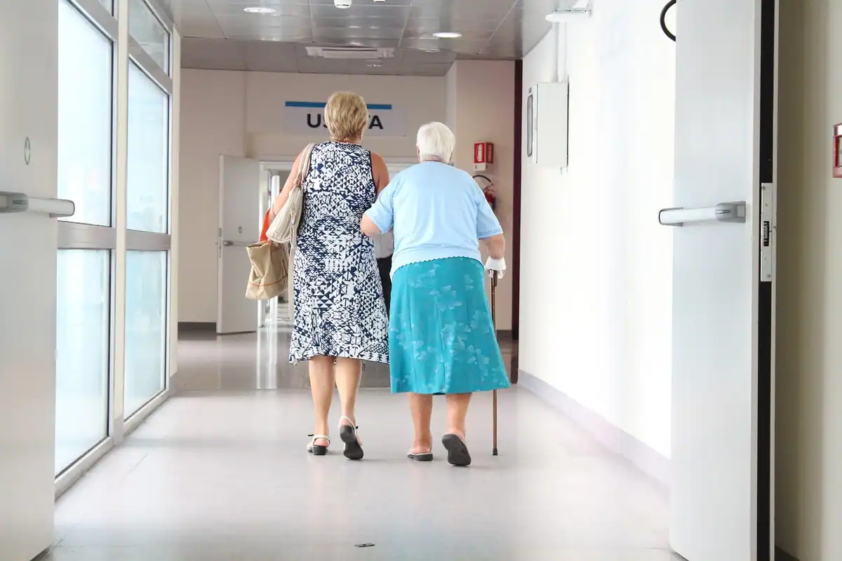Două femei în vârstă merg încet pe holul unui spital