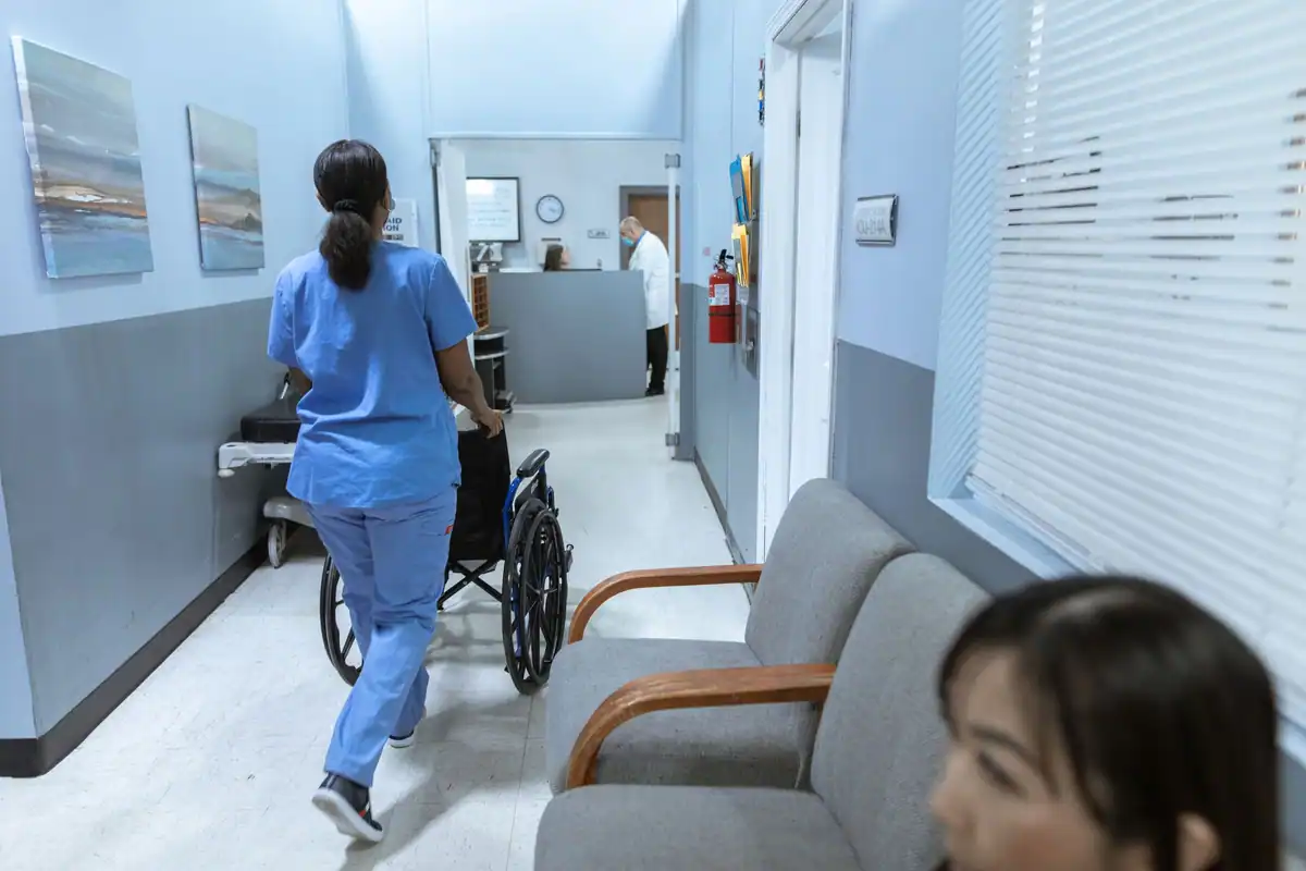 Asistentă împinge un scaun cu rotile pe coridorul unui spital