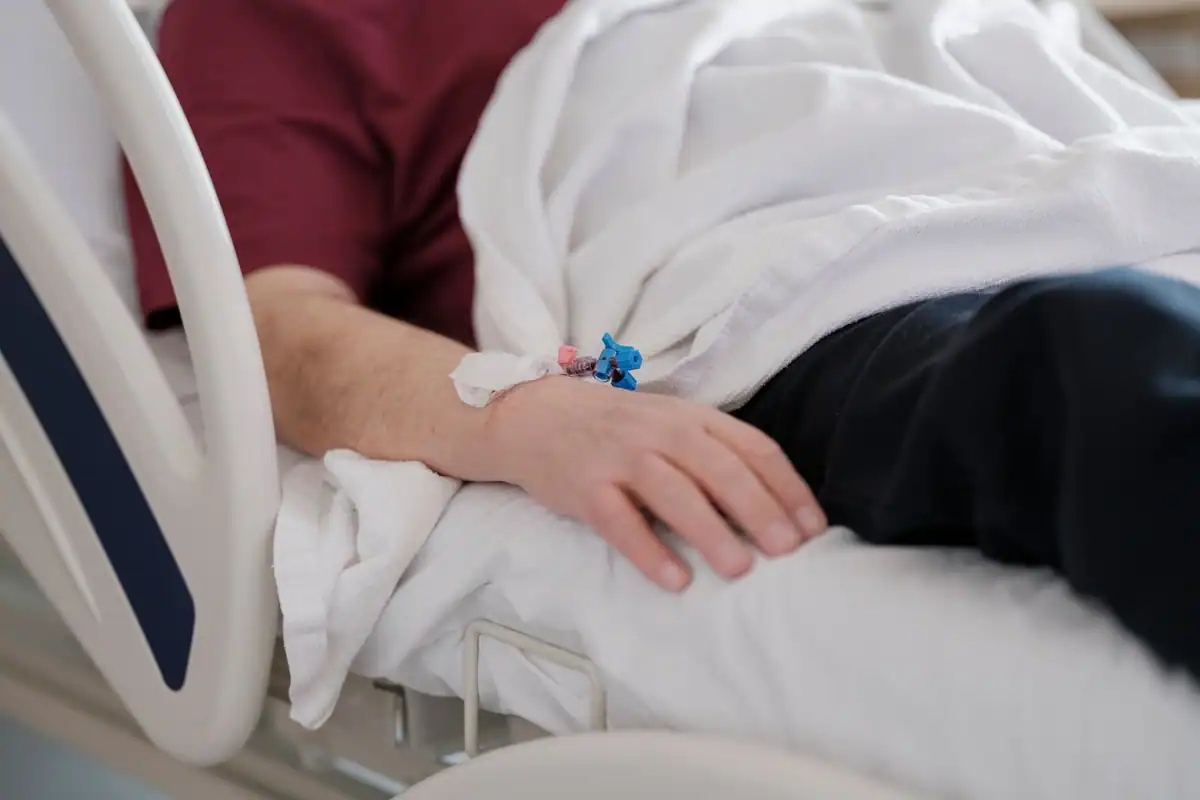 Pacient în pat de spital, cu un cateter pentru perfuzie la mână