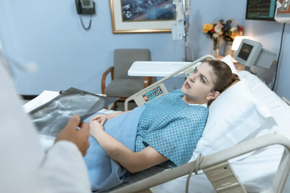 Pacientă în pat privește o radiografie ținută de un medic, în salon